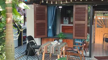 A room with a patterned floor, a table with a patterned tablecloth, two chairs, a small potted plant, and a window with wooden shutters.