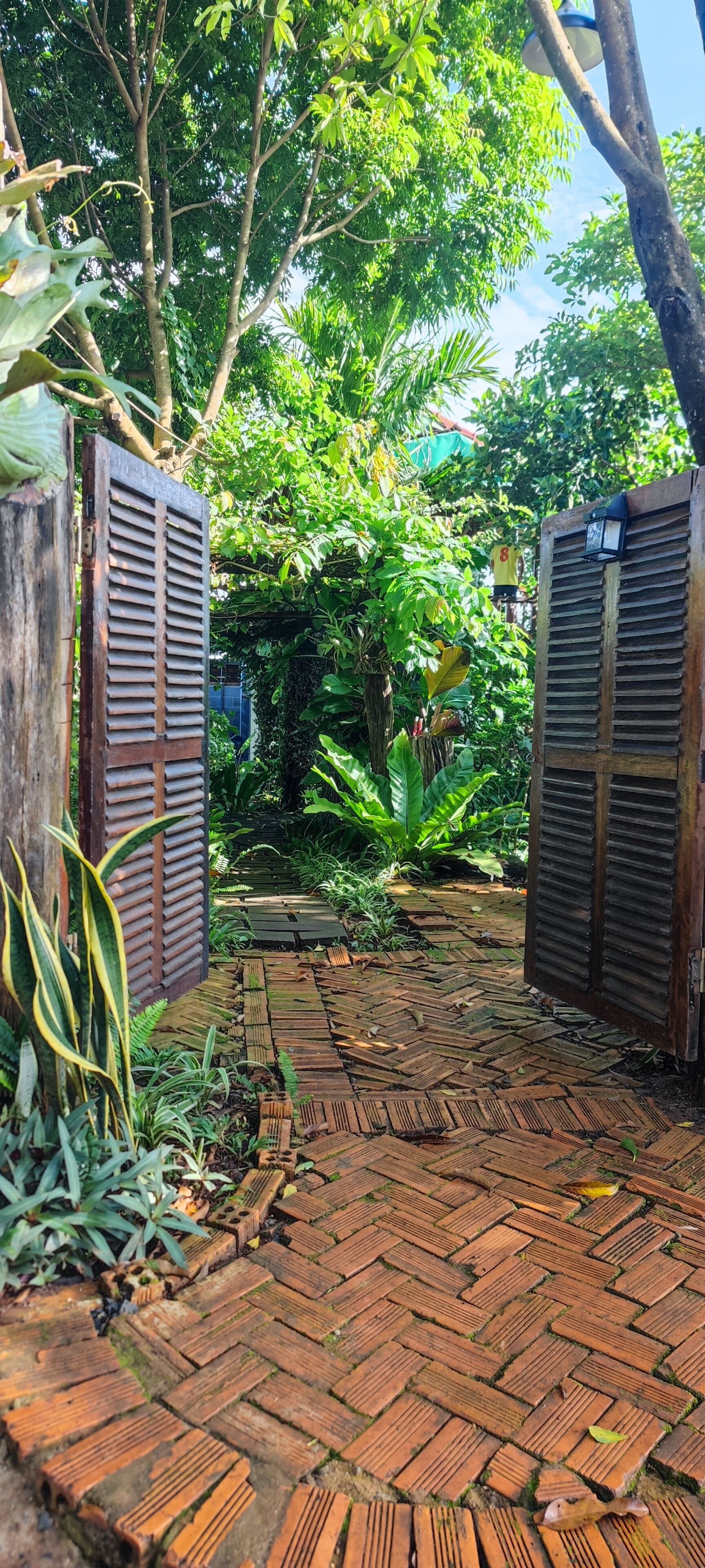 Un sendero en un jardín con diseño de ladrillo que conduce a un portón de madera.