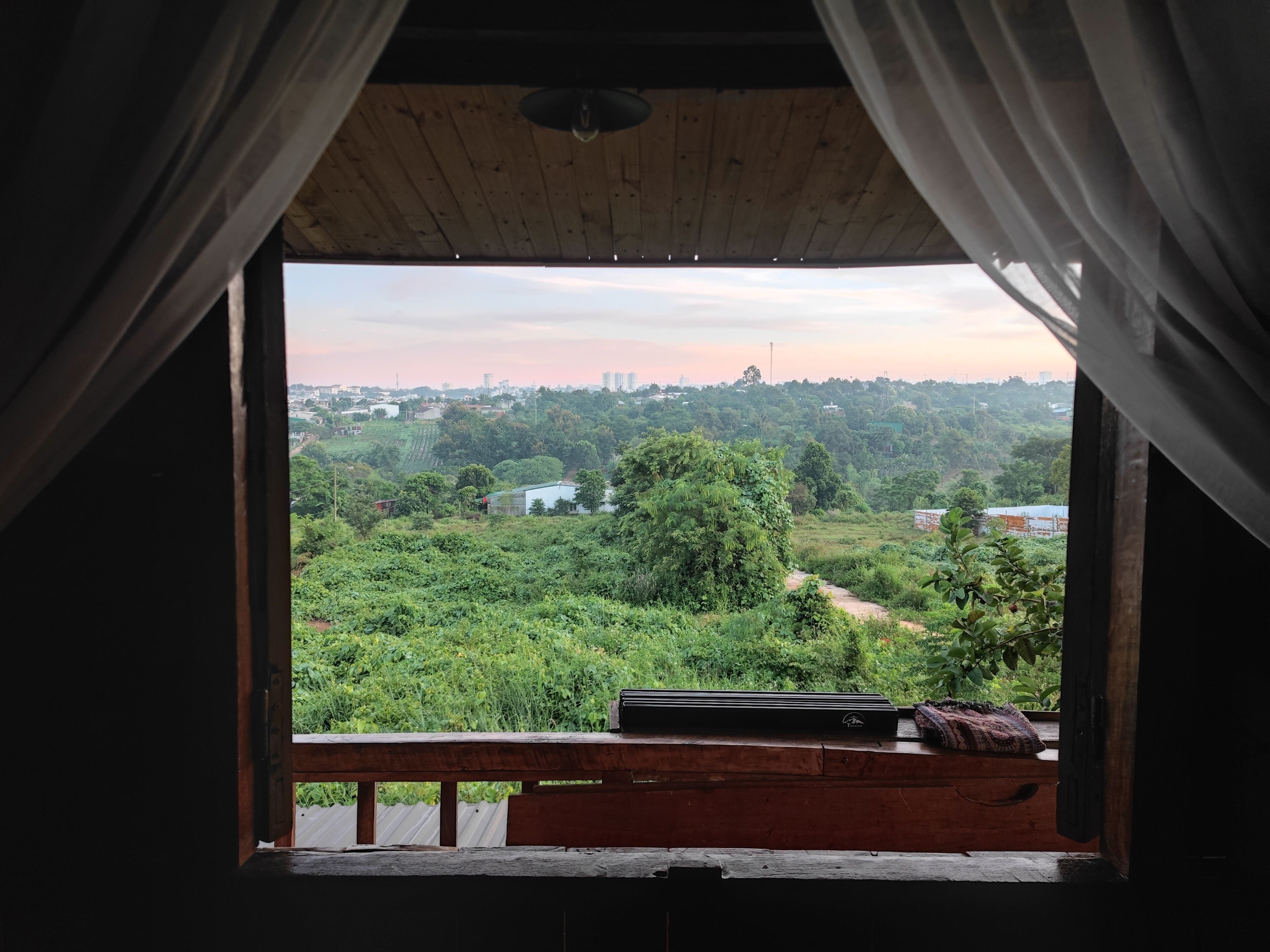 A room with a view of a green landscape, a wooden ceiling, and a window with curtains.