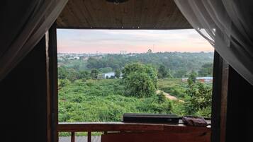 A room with a view of a green landscape, a wooden ceiling, and a window with curtains.