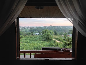 A room with a view of a green landscape, a wooden ceiling, and a window with curtains. - Natural Garden BMT: Trải nghiệm nguyên căn riêng tư giữa vườn sinh thái 160m (Ea Kao)