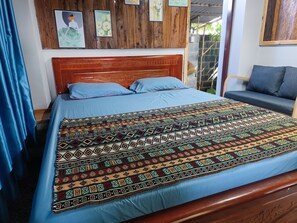 A bed with a patterned bedspread, a wooden headboard, and a blue pillow. - Natural Garden BMT: Trải nghiệm nguyên căn riêng tư giữa vườn sinh thái 160m (Ea Kao)