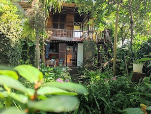 A wooden house with a porch, surrounded by lush greenery and plants. - Natural Garden BMT: Trải nghiệm nguyên căn riêng tư giữa vườn sinh thái 160m (Ea Kao)