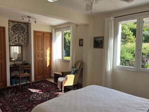 Ein Schlafzimmer mit Bett, Stuhl, Schreibtisch, Kleiderschrank und einem Fenster mit Blick auf Grünflächen.