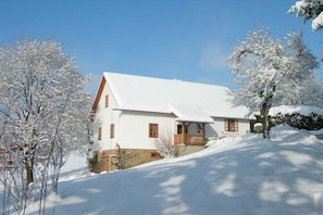 A white building with a sloped roof, surrounded by snow-covered trees.