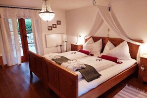 Ein Doppelbett mit Holzrahmen, weißen Bettwäsche und einem Baldachin. Ein Nachttisch mit Lampe, ein kleiner Schrank mit herzförmigem Griff und ein weiterer Nachttisch mit Lampe sind vorhanden.