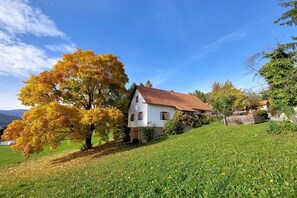 Ein weißes Haus mit rotem Dach, umgeben von einer grünen Wiese und Bäumen mit Herbstlaub.