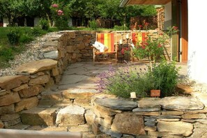 A stone pathway leading to a seating area with a chair and a table, surrounded by plants and a stone wall.