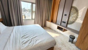 A hotel room with a bed, curtains, a wall-mounted TV, and a small trash bin. - Hotel Ishant (Dwarka)