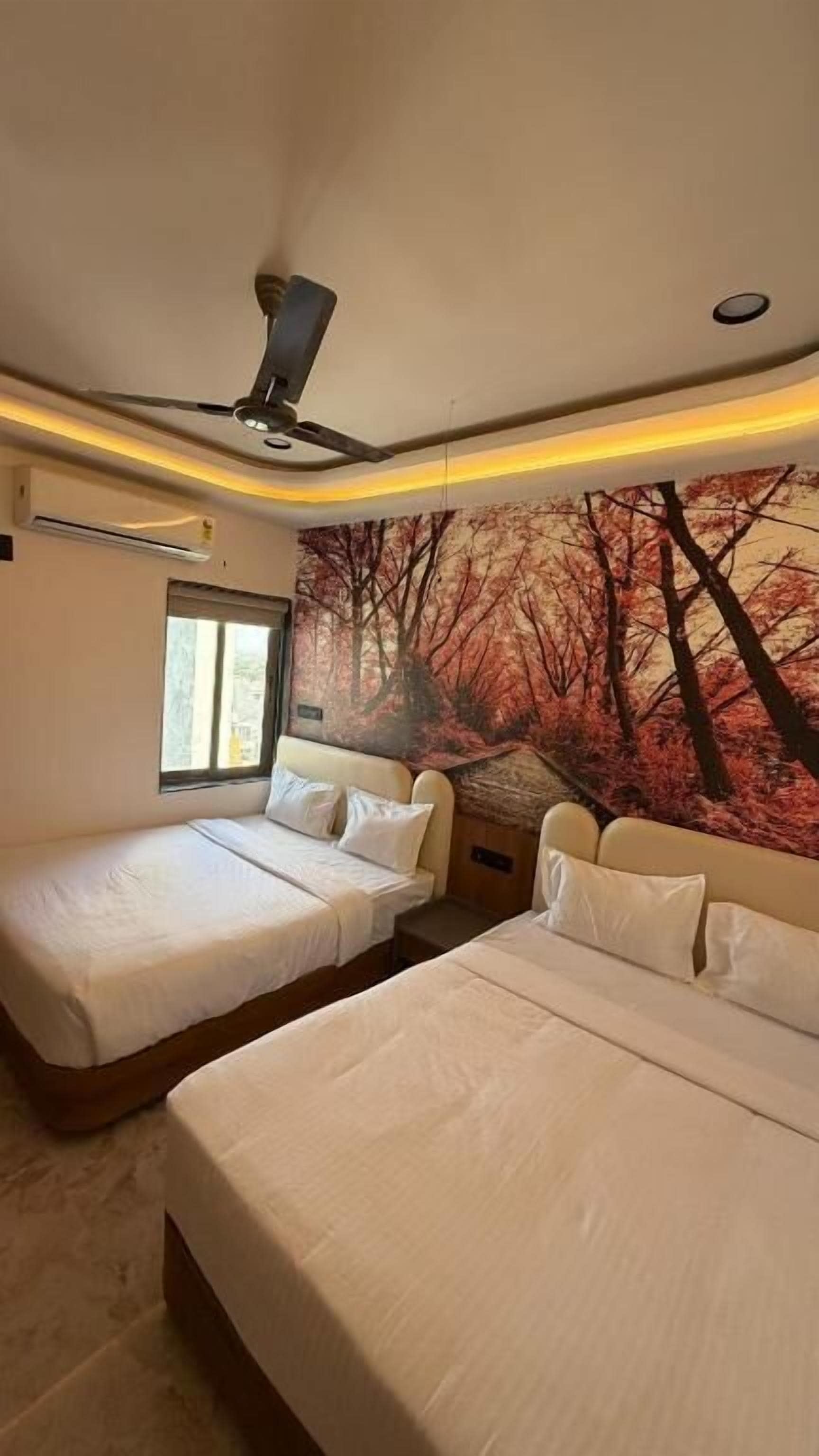 Quarto de hotel com duas camas, um ventilador de teto, uma janela e um mural na parede.