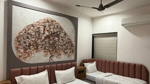 A hotel room with a large bed, a smaller bed, a ceiling fan, and a wall-mounted air conditioner. - Hotel Ishant (Dwarka)