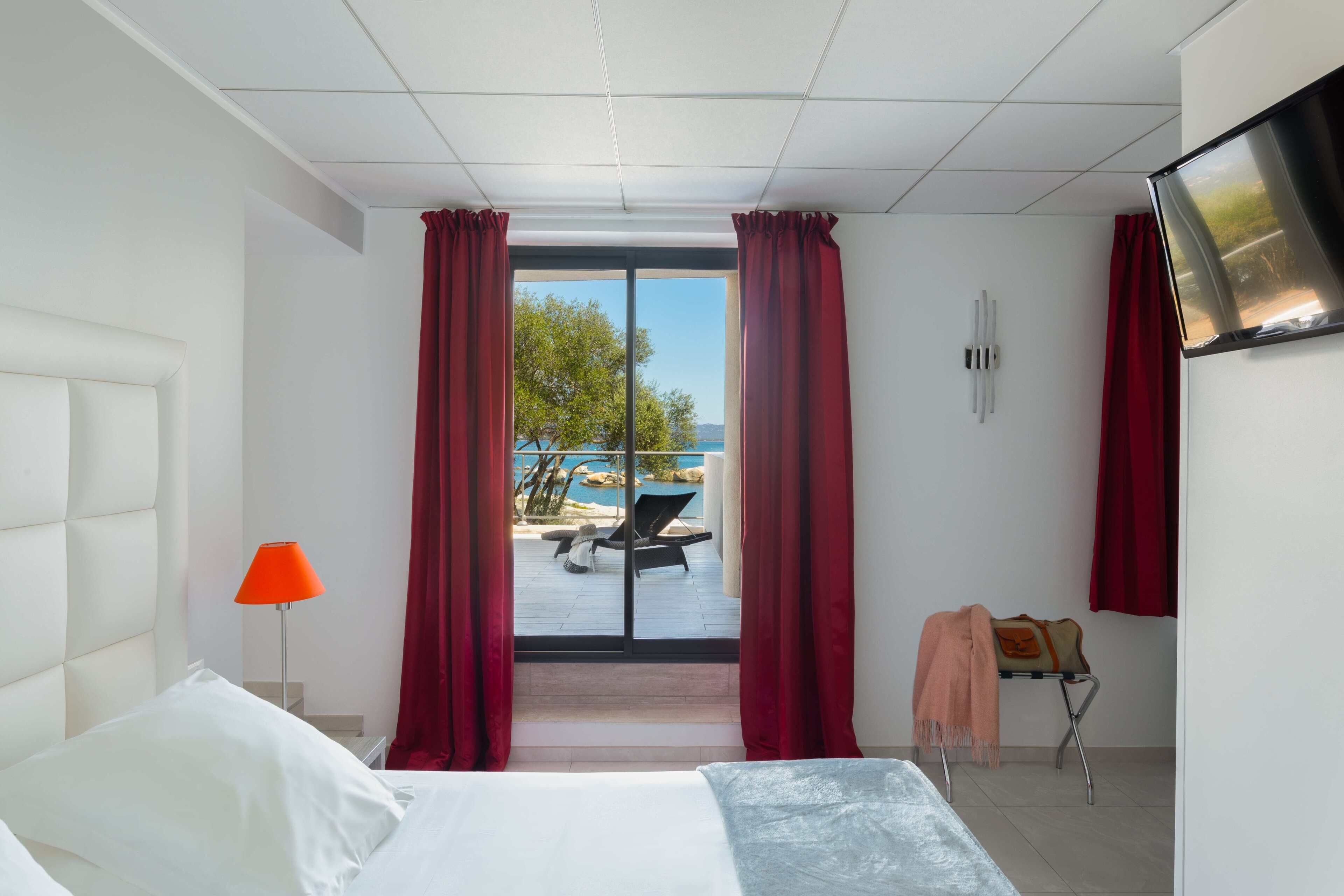 Une chambre d’hôtel équipée d’un lit, d’un bureau, d’une chaise, d’une télévision et offrant une vue sur un espace extérieur comprenant une piscine et des chaises longues.