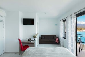 A modern bedroom with a bed, a desk, a red chair, a TV, a sofa, and a view of the sea. - LES ROCHES BLANCHES (Porto-Vecchio)