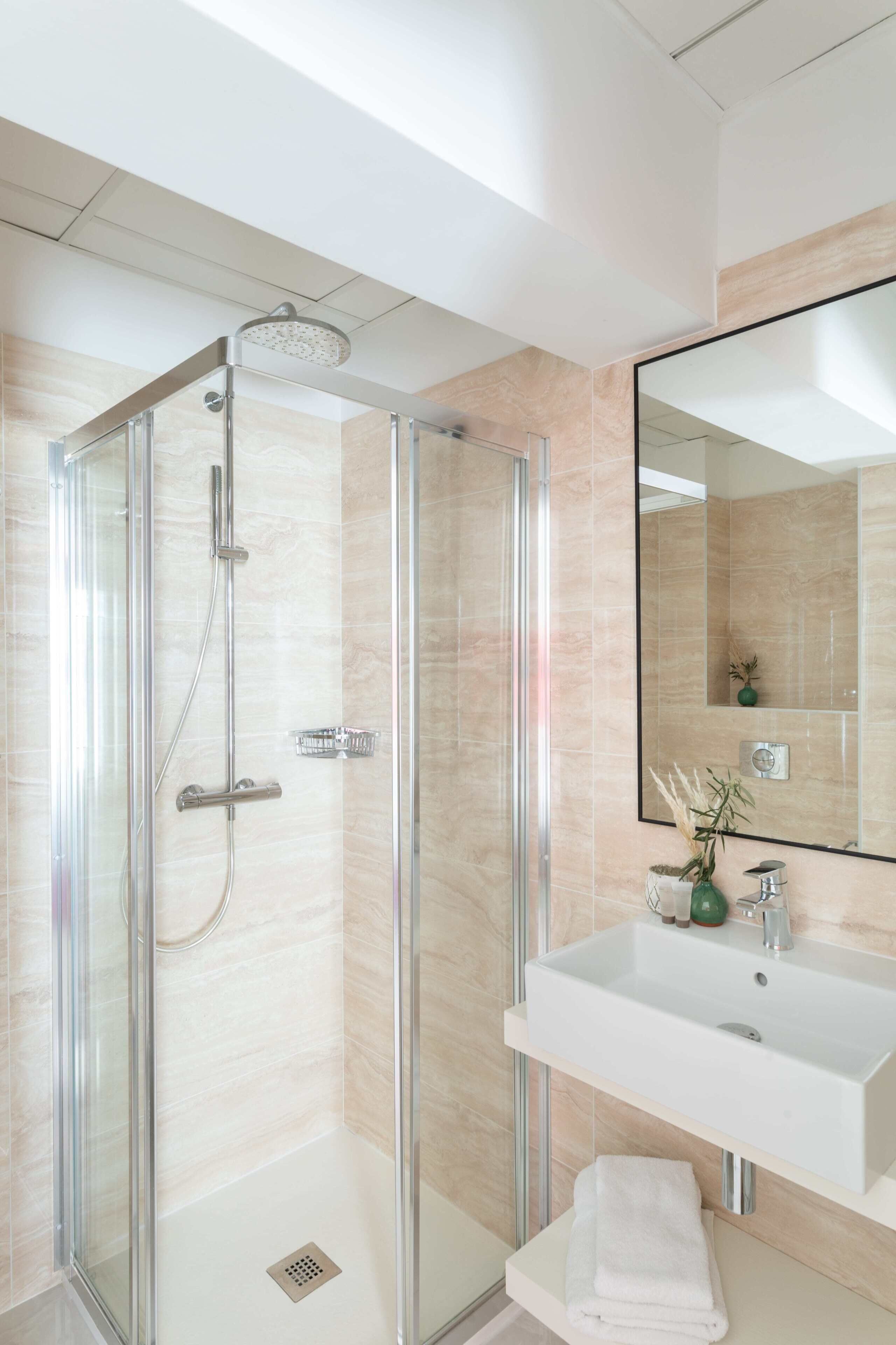 Een moderne badkamer met een douchecabine van glas, een witte wastafel en een spiegel.