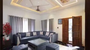 A modern living room with a sectional sofa, a glass coffee table, and a wooden door. - Alleppey Breeze by 8MH - Luxury Backwater Villa (Mararikulam)