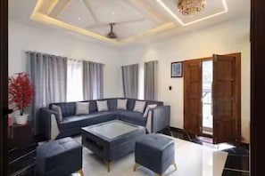 A modern living room with a sectional sofa, a glass coffee table, and a wooden door. - Alleppey Breeze by 8MH - Luxury Backwater Villa (Mararikulam)