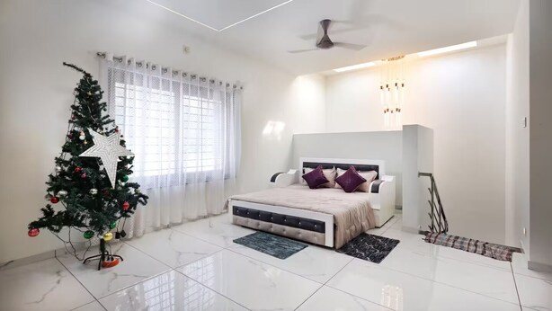 A modern bedroom with a bed, a Christmas tree, and a ceiling fan. - Alleppey Breeze by 8MH - Luxury Backwater Villa (Mararikulam)