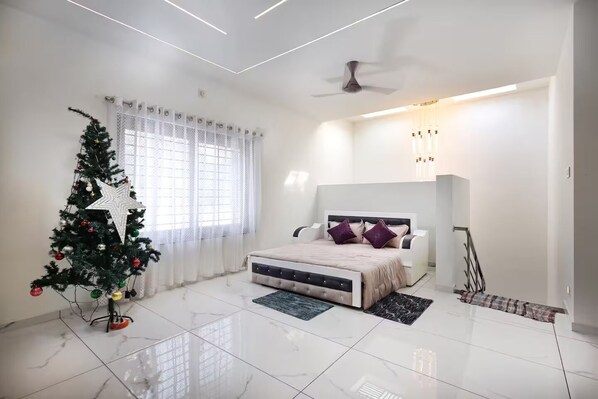 A modern bedroom with a bed, a Christmas tree, and a ceiling fan. - Alleppey Breeze by 8MH - Luxury Backwater Villa (Mararikulam)