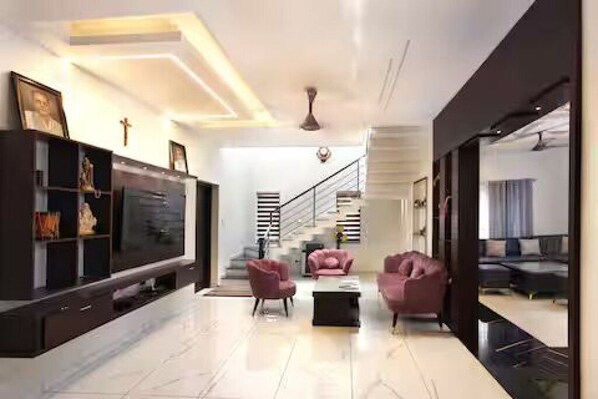 A modern living room with a flat-screen TV, a staircase, and a sofa.
