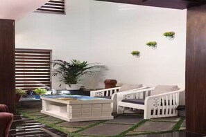 A room with a white sofa, a coffee table, a potted plant, and a wall-mounted shelf with small plants.