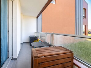 A balcony with a wooden table and chairs, a blue curtain, and a view of a building. - A Stopover at Juno - Balcony 100 meters from the beach (Courseulles-sur-Mer)