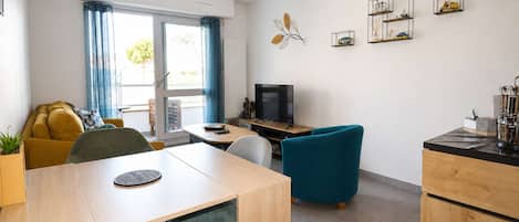 A modern living room with a dining area, a television, and decorative wall art.