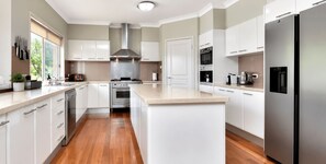 A modern kitchen with white cabinets, stainless steel appliances, and a wooden floor.