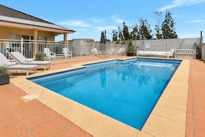 A rectangular swimming pool with a tiled edge, surrounded by a white fence.