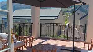 Ein überdachter Außenbereich mit Tisch und Stühlen, einem großen Sonnenschirm und Blick auf die umliegende Landschaft.