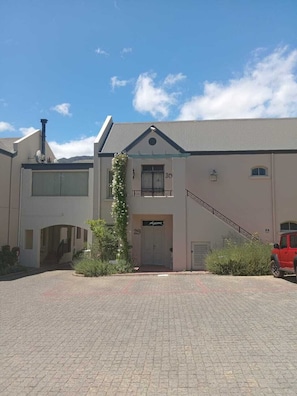 Een gebouw met twee verdiepingen, een centrale ingang, een trap en een rood voertuig dat er geparkeerd staat.