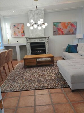 Een woonkamer met een open haard, een bank, een salontafel en twee schilderijen aan de muur.