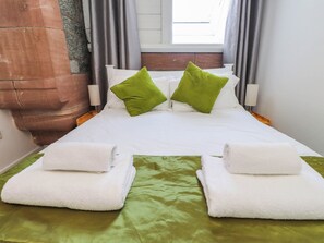 A bed with white bedding, green pillows, and two white towels on a green bedspread. - Cecily's Retreat (Criccieth)