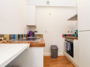A compact kitchen with a sink, a kettle, a trash bin, and a stove. - Cecily's Retreat (Criccieth)
