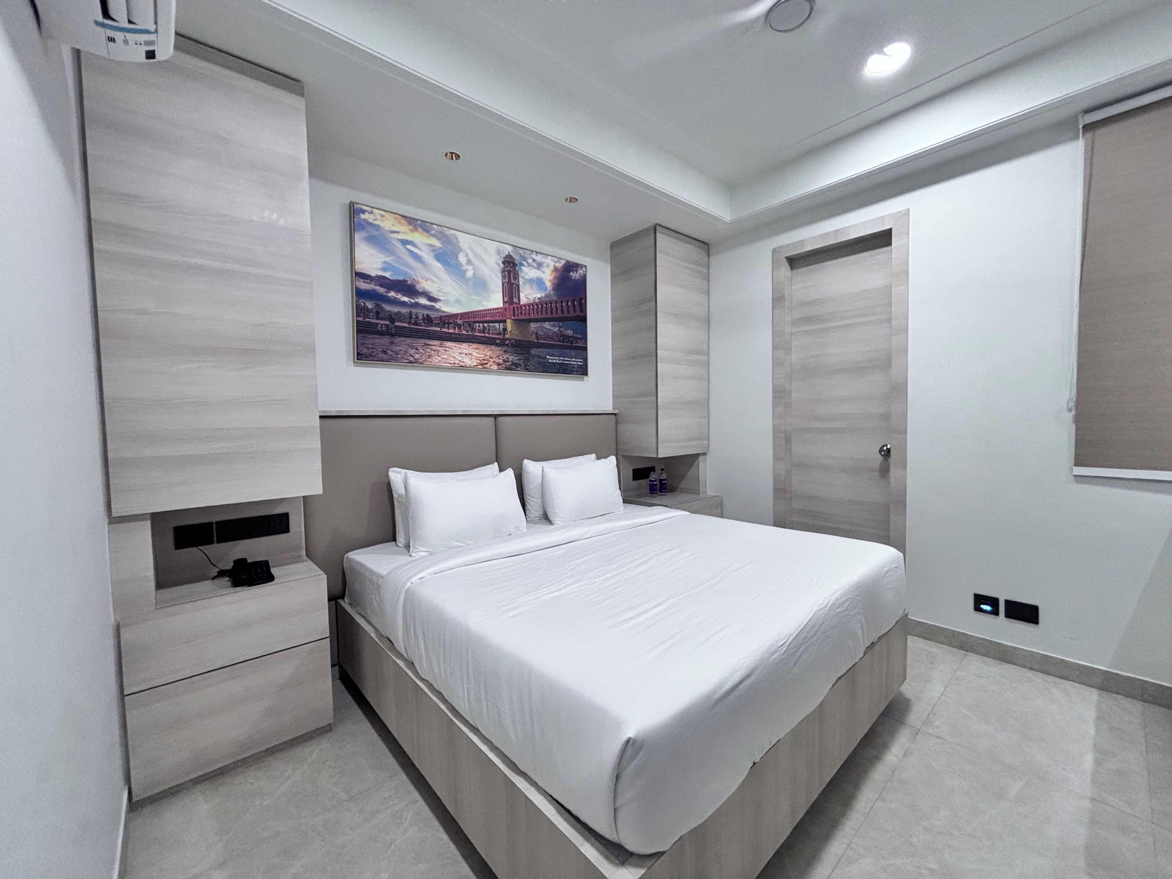 A modern bedroom with a large bed, built-in storage, a painting of a bridge, and a wardrobe.