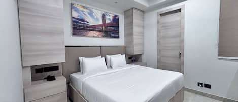 A modern bedroom with a large bed, built-in storage, a painting of a bridge, and a wardrobe.