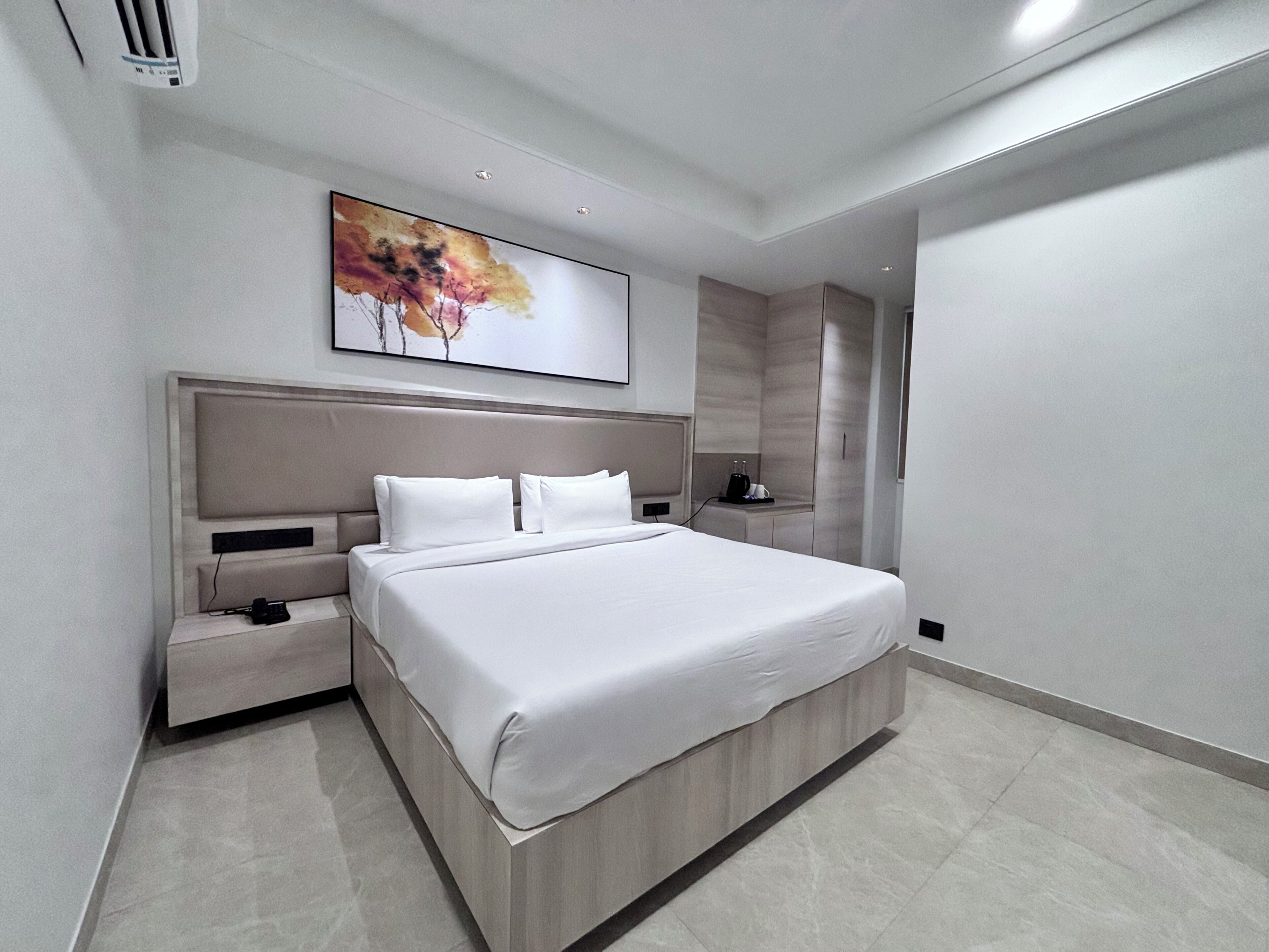 Una habitación de hotel moderna con una cama grande, mesitas de noche, un armario empotrado y una obra de arte en la pared.