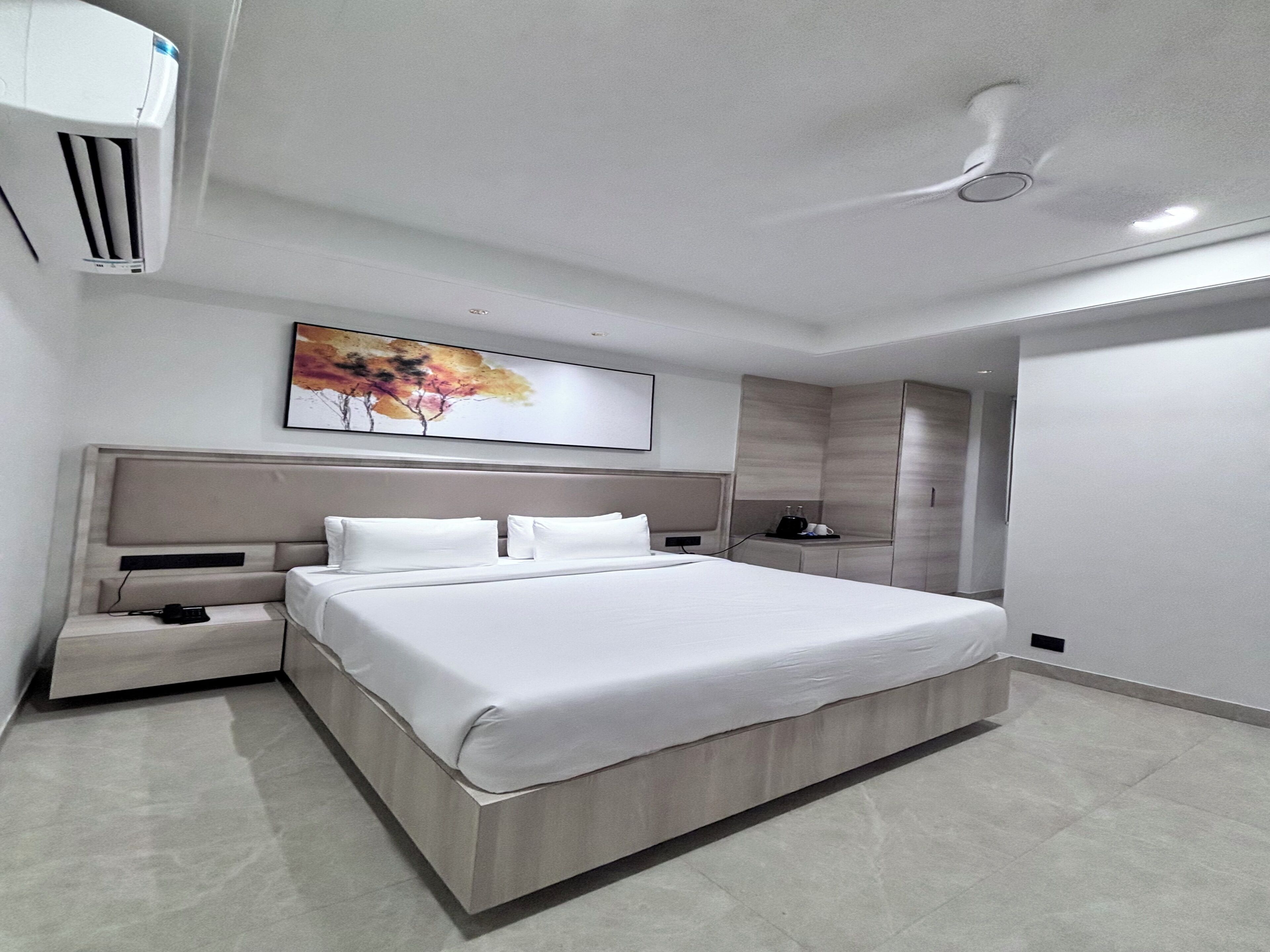 Habitación de hotel moderna con una cama grande, mesitas de noche, un televisor de pantalla plana, un ventilador de techo y un cuadro en la pared.