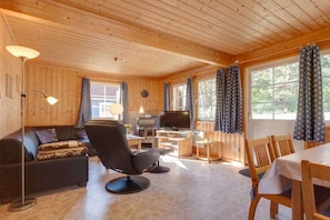 A cozy cabin interior with a sofa, a chair, a dining table, a TV, and a fireplace. - Swedish House Red Water Lily (Userin)
