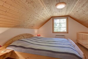 A bedroom with a sloped ceiling, a bed with a striped blanket, a nightstand, a crib, and a window. - Swedish House Red Water Lily (Userin)