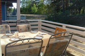 An outdoor dining area with a table set for four, surrounded by metal chairs, overlooking a wooded area. - Swedish House Red Water Lily (Userin)