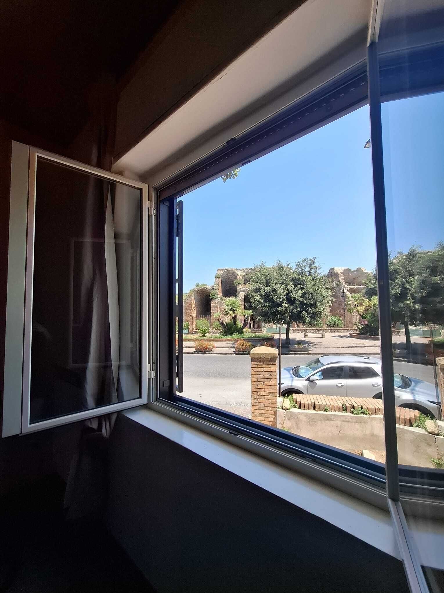 Janela com vista para área externa, incluindo estacionamento e vegetação.