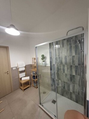 Ein Badezimmer mit einer Duschkabine, einem Holzstuhl, einem Handtuchregal und einem Topf mit einer Pflanze.