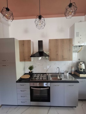 Cozinha moderna com fogão a gás, forno e pia de aço inoxidável. Possui armários de madeira, coifa preta e luminárias pendentes.