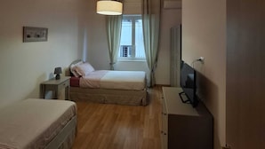 A compact hotel room with a single bed, a bedside table, a desk with a chair, a television, and a window with curtains. - Vrbo Property (Pozzuoli)