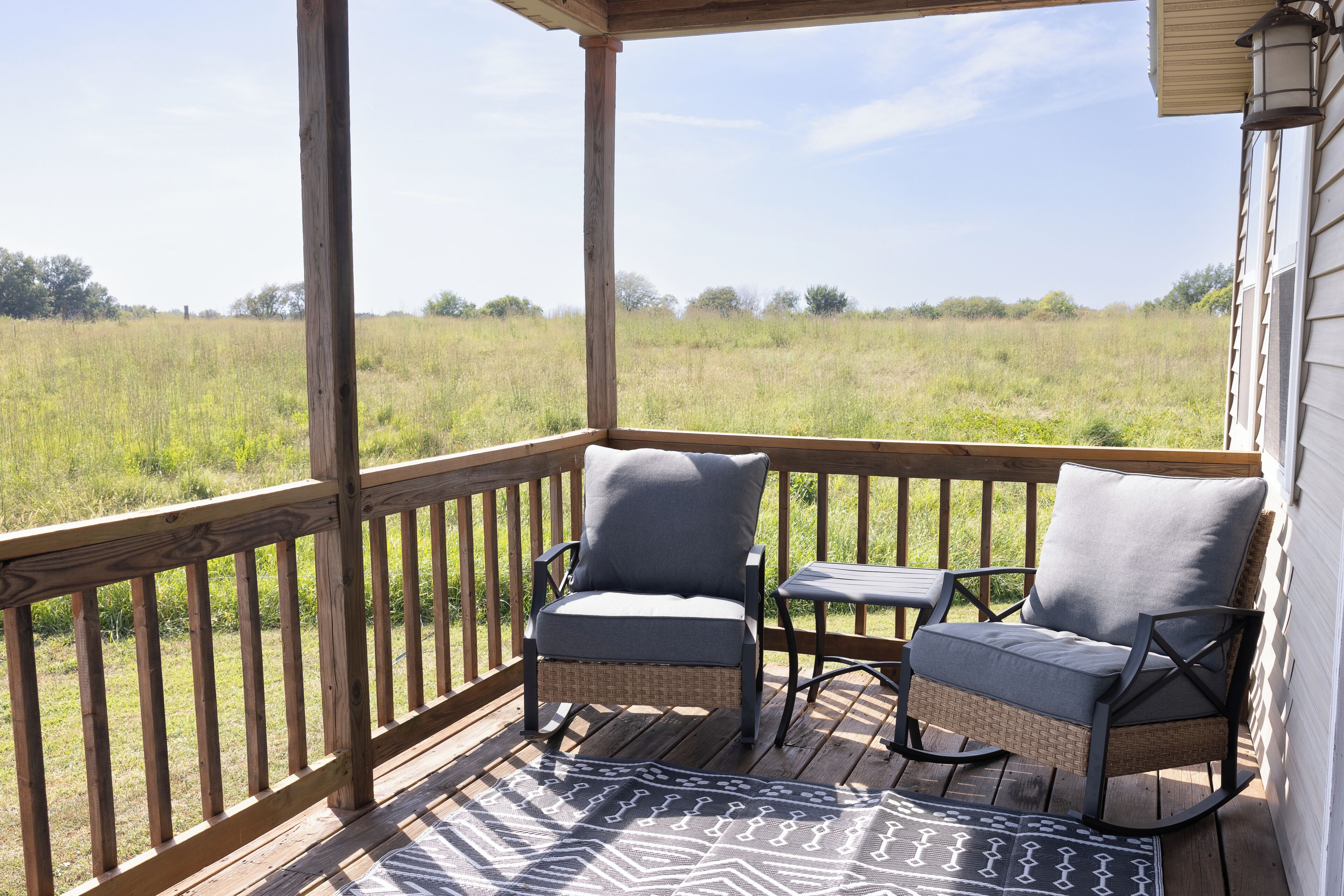 A wooden deck with two wicker chairs and a small table, overlooking a grassy field.
