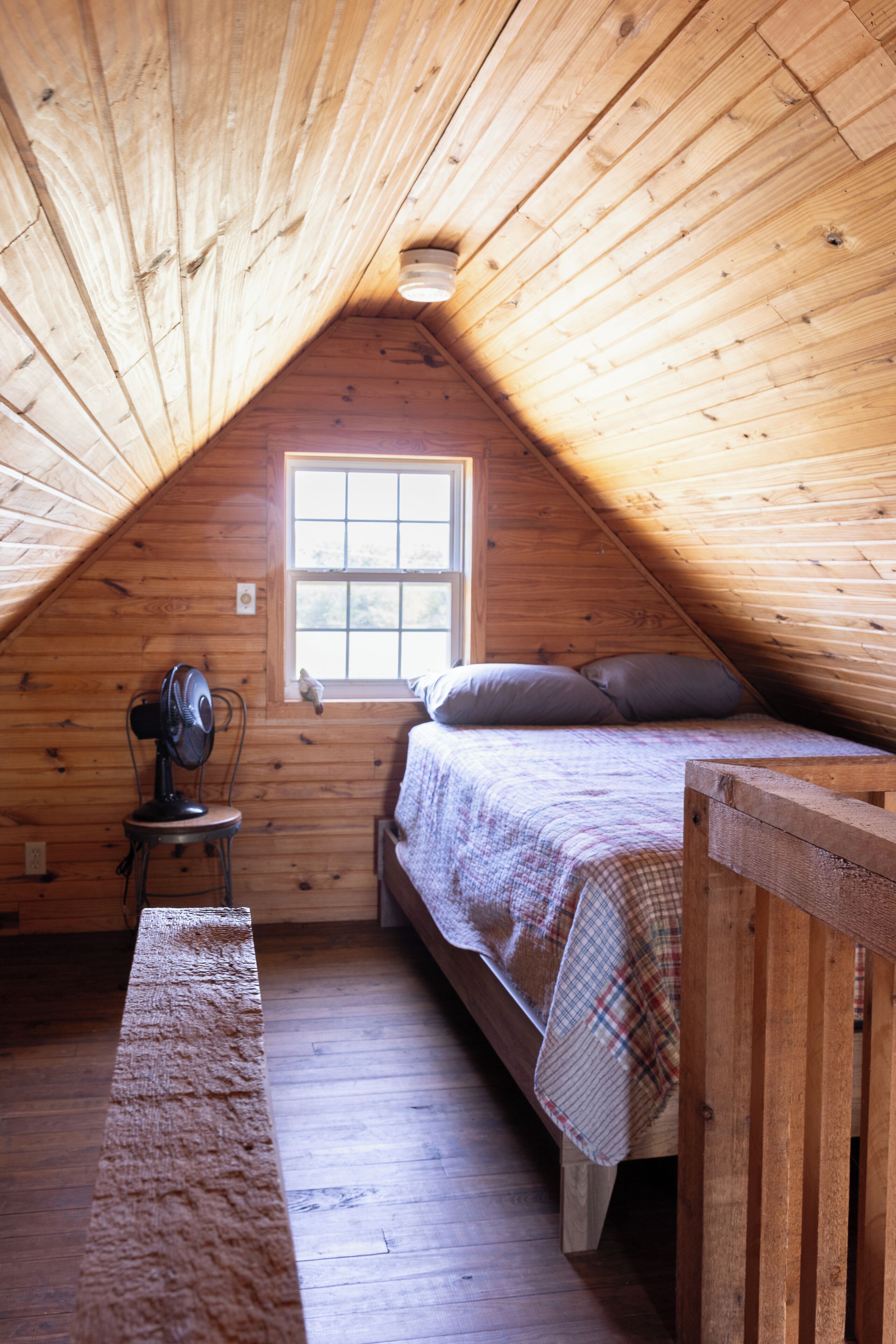 A small, attic-style bedroom with a single bed, a window, and a fan.