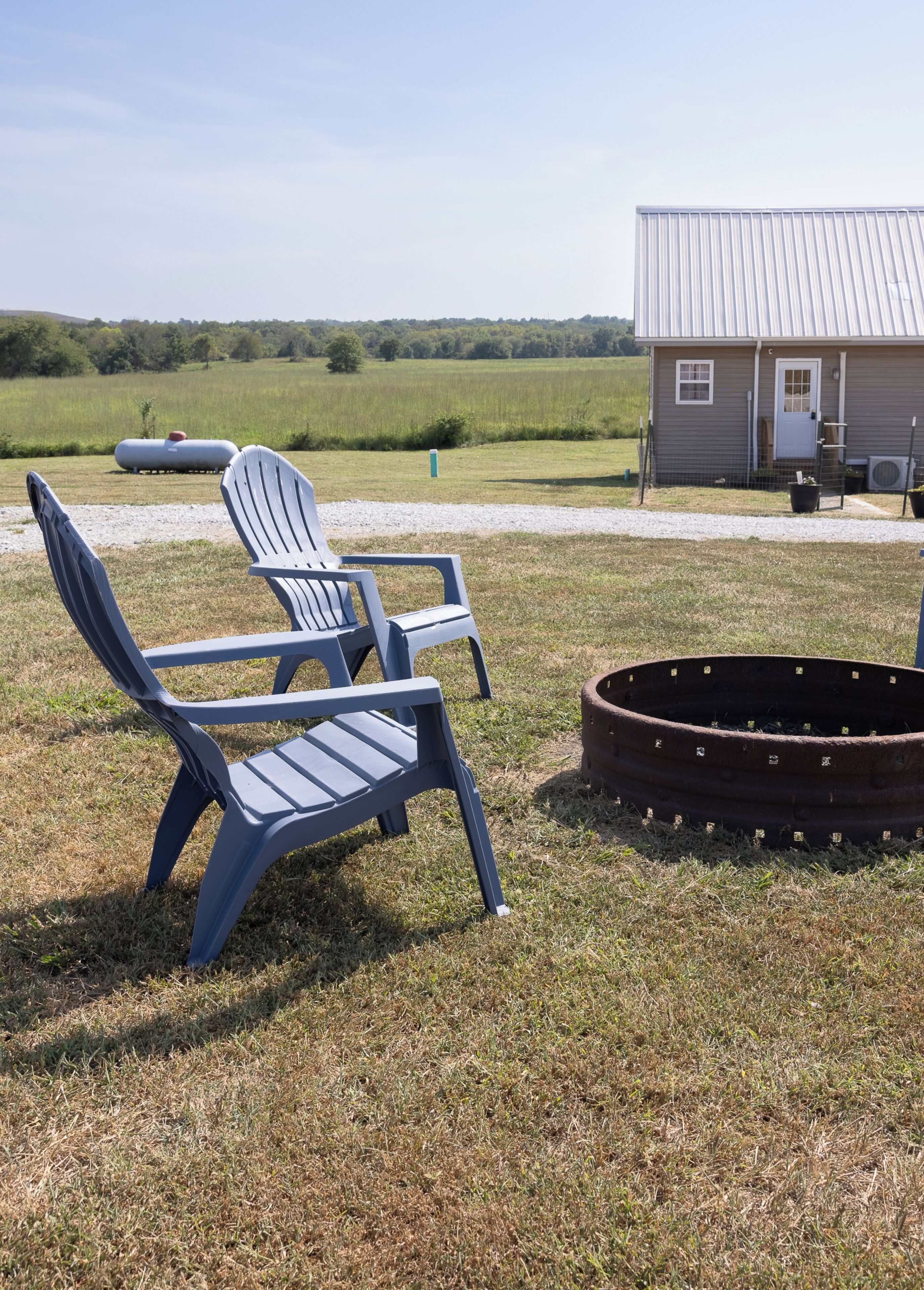 A grassy outdoor area with two Adirondack chairs and a fire pit.