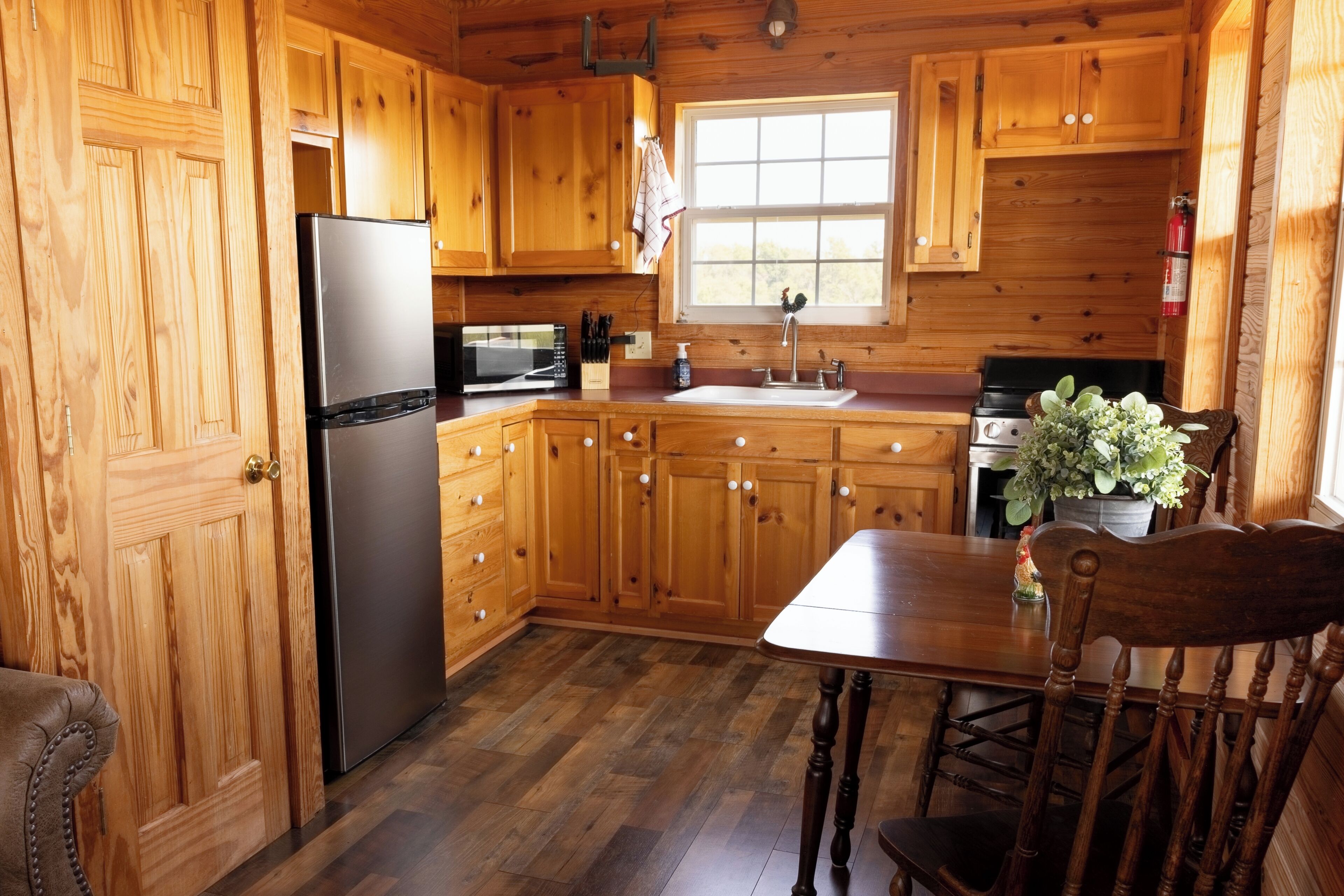 A wooden cabin kitchen with a refrigerator, microwave, sink, and stove.