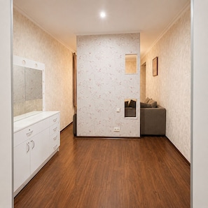 Een kamer met een houten vloer, een witte dressoir met lades, een grijze bank en behang met een patroon.