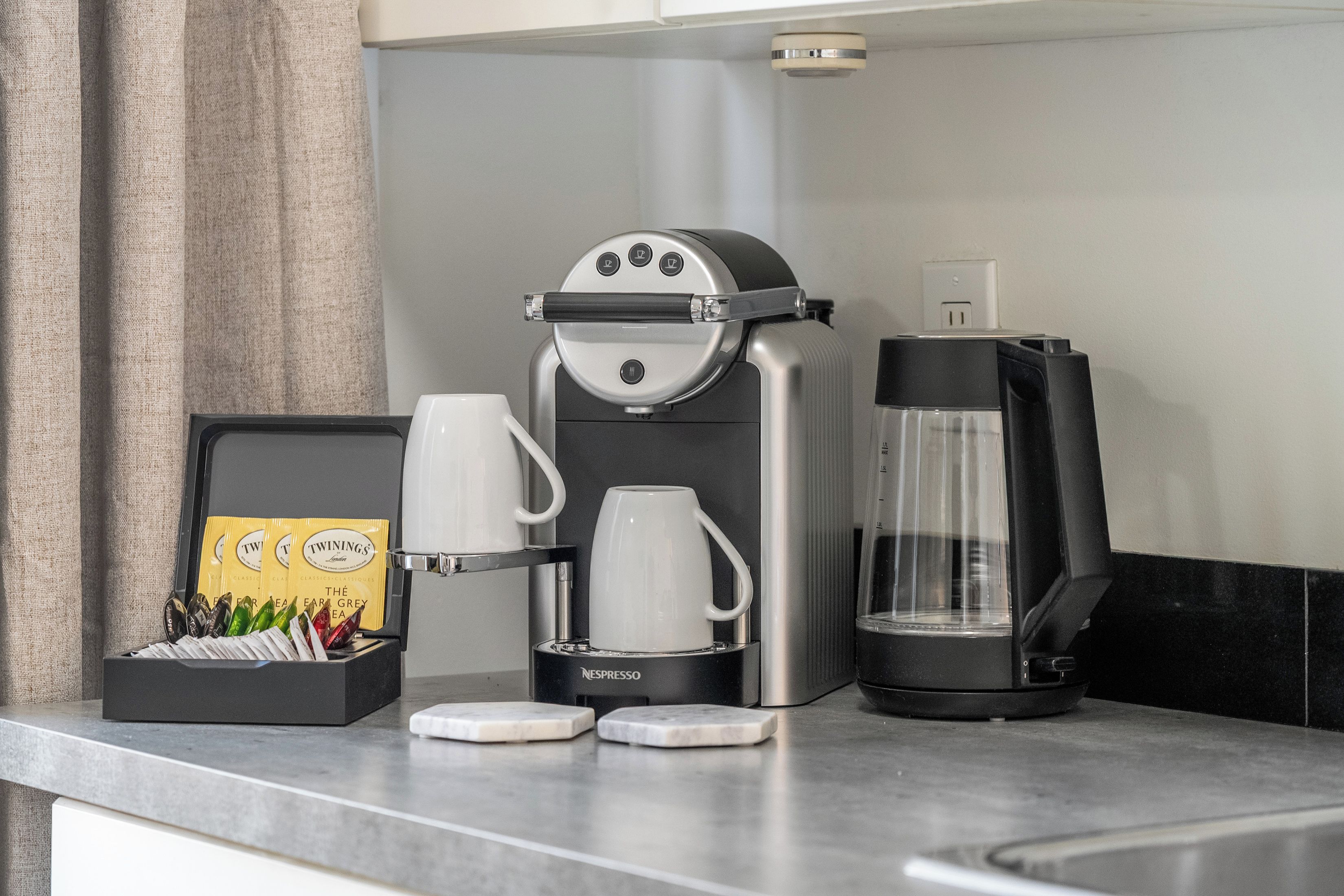 A kitchenette with a coffee maker, a tea kettle, and a glass carafe on the counter.